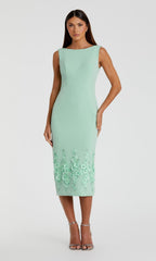 A woman wears the Mac Duggal 11853 Midi Sheath Wedding Guest Dress in mint green, featuring a fitted silhouette and floral appliqué at the hem, paired with silver heels for a chic wedding guest look.