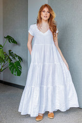 Woman wearing white bohemian linen dress with V-neck and tiered skirt standing indoors near plant