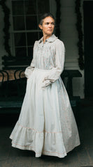 Photo of woman standing outdoors wearing prairie dress. Model is truning and skirt is full. Hands are in the pockets of the apron.