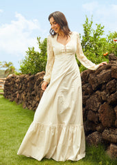 Woman in a white dress standing outdoors near a stone wall with greenery in the background