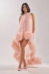 A woman poses confidently in the ARI TULLE RUFFLE HIGH LOW MINI DRESS IN BLUSH, featuring dramatic sheer trim, paired with matching pink satin ballet-style heels against a plain light background.