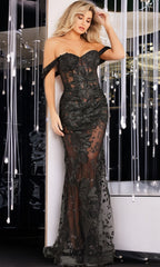 A woman in the Jovani Sexy Sheer Long Black Formal Dress 23920, featuring off-the-shoulder styling, sheer mesh panels, and floral embroidery, stands by a wall adorned with hanging string lights.