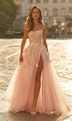 A woman stands on a sunlit cobblestone street wearing the La Femme 33432 long prom dress in light pink, featuring a strapless neckline, high slit, and floral appliqué.