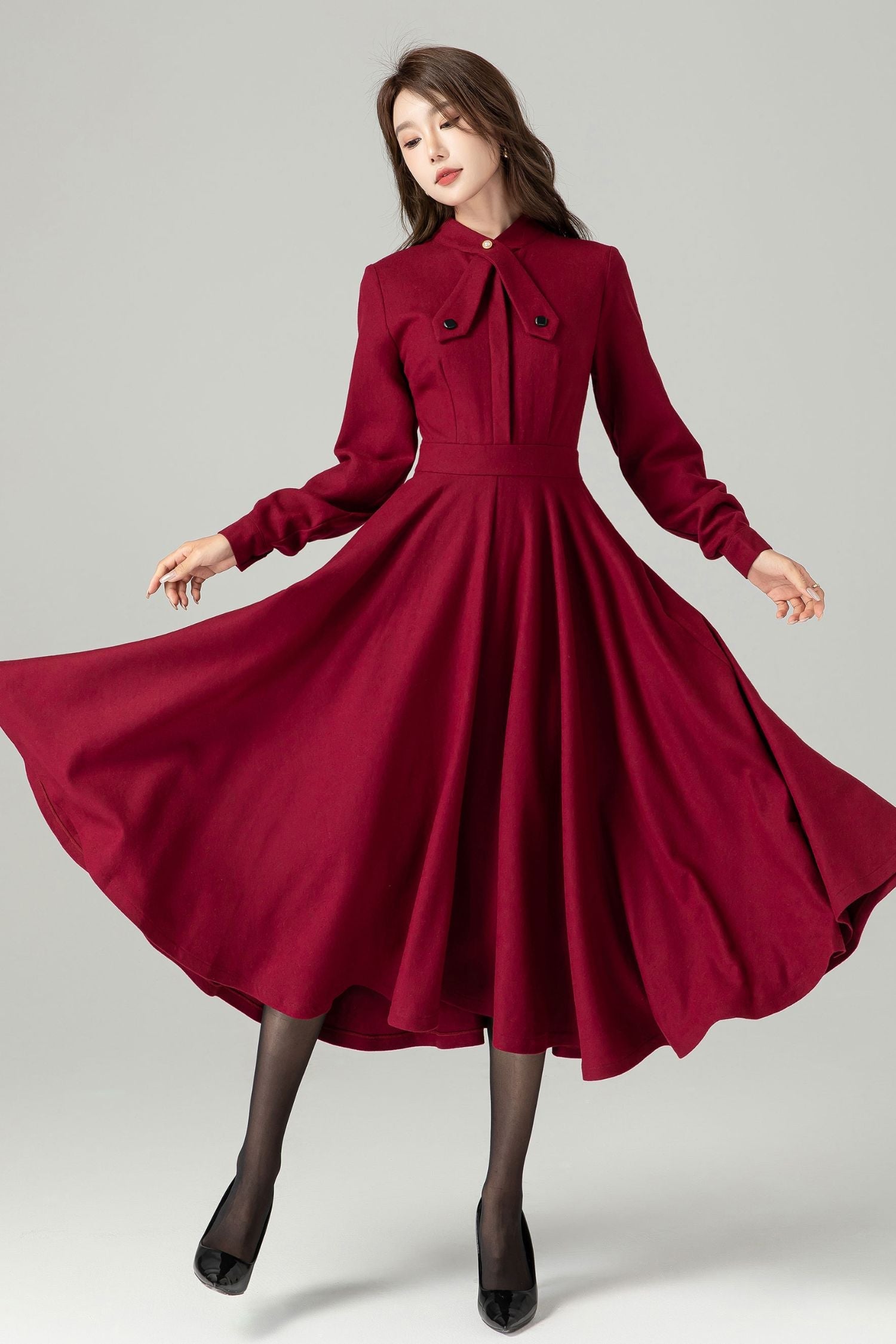A woman in a red vintage-inspired wool dress with a fitted waist and flared skirt, featuring a satiny lining and long sleeves with button closure.