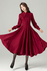 A woman in a red vintage-inspired wool dress with a fitted waist and flared skirt, featuring a satiny lining and long sleeves with button closure.