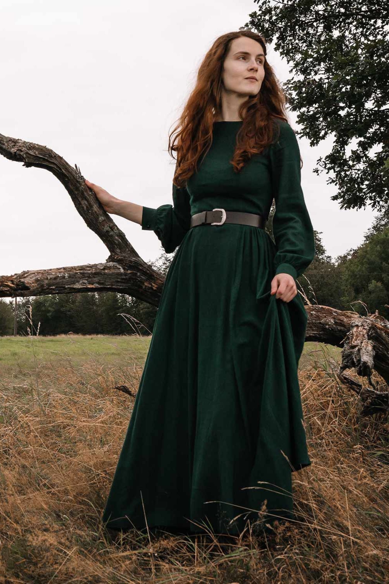 A person wearing a green linen maxi dress with long sleeves, standing next to a tree in an outdoor setting.