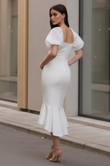Woman in a white dress standing on a street in front of a modern building.
