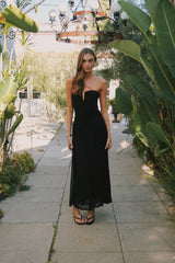 black-image | Woman in a black dress standing in a garden setting with plants and a chandelier.