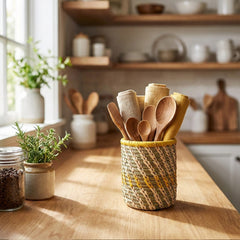 Kitchen counter with woven utensil holder and wooden spoons, shelves with kitchenware in the background.