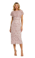 A woman wears the Mac Duggal Beaded Midi Wedding-Guest Dress 94117 in light pink, featuring short sleeves and sequin embellishments, styled with nude high-heeled sandals.