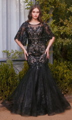 A woman stands outdoors before green foliage, wearing the Andrea & Leo A1377 Black Lace Mermaid Prom Dress with sequins, sheer sleeves, and a flared tulle skirt.
