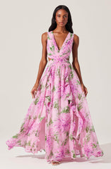 A woman is wearing a sleeveless, V-neck, floor-length dress with a pink floral pattern. The dress has cutouts at the waist and features a flowing, layered skirt with ruffles. The fabric is lightweight and sheer, creating an elegant and airy appearance.
