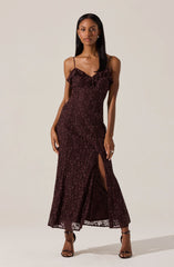 A woman is wearing a long, burgundy lace dress with spaghetti straps and a ruffled neckline. The dress features a high slit on one side, revealing her leg. She is also wearing black open-toe high-heeled sandals.