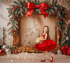 Young girl in a red dress holding a gift box, surrounded by Christmas decorations including a large framed wreath with a red bow.