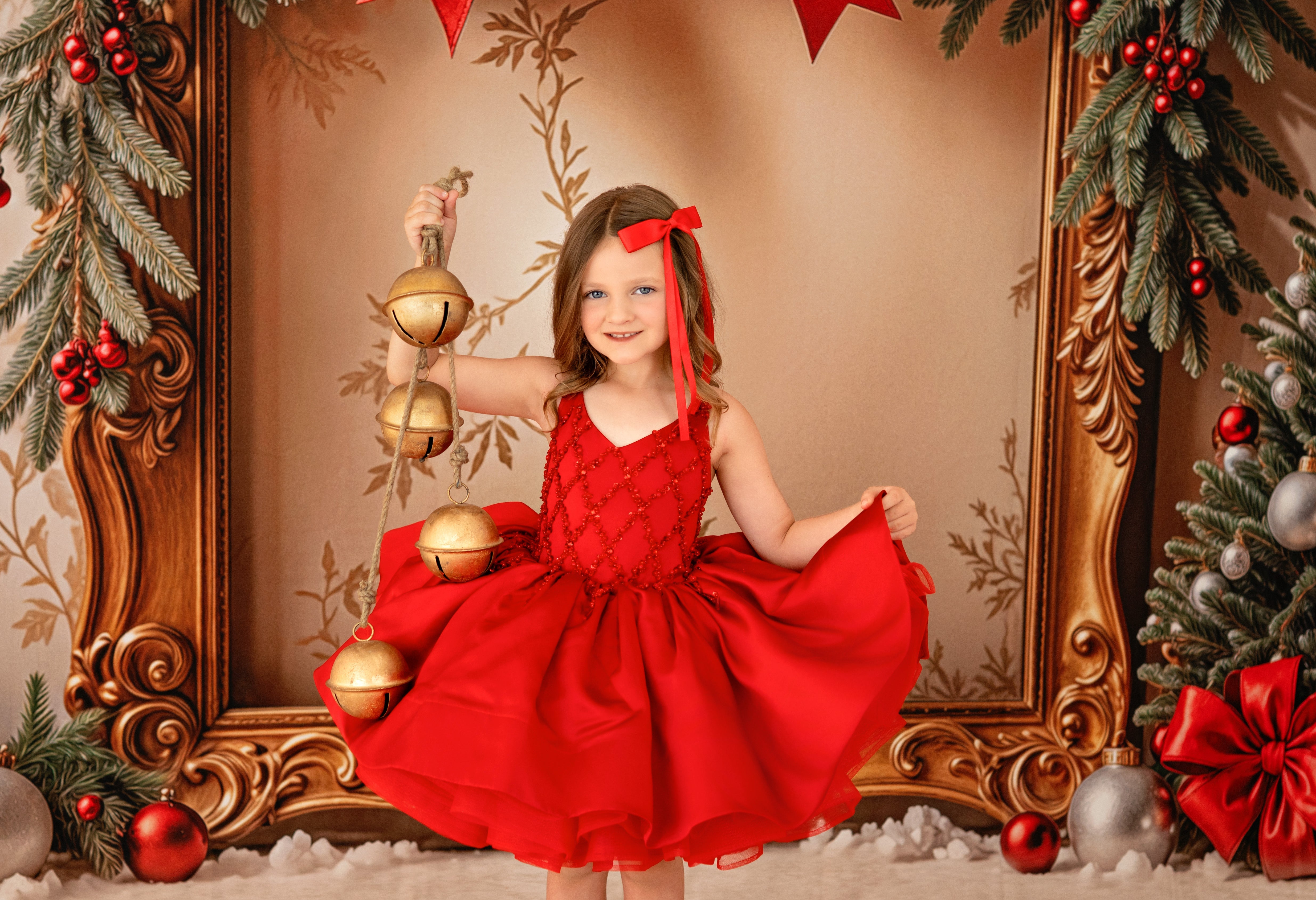 Young girl in a red dress holding Christmas ornaments in a decorated setting with a gold frame and festive decorations.