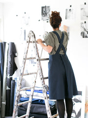 Woman wearing the Apron Dress sewing pattern by The Assembly Line. A pinafore style dress pattern made in denim, cotton twill or canvas fabric featuring cross over back straps, large front pockets and button pleat back opening.