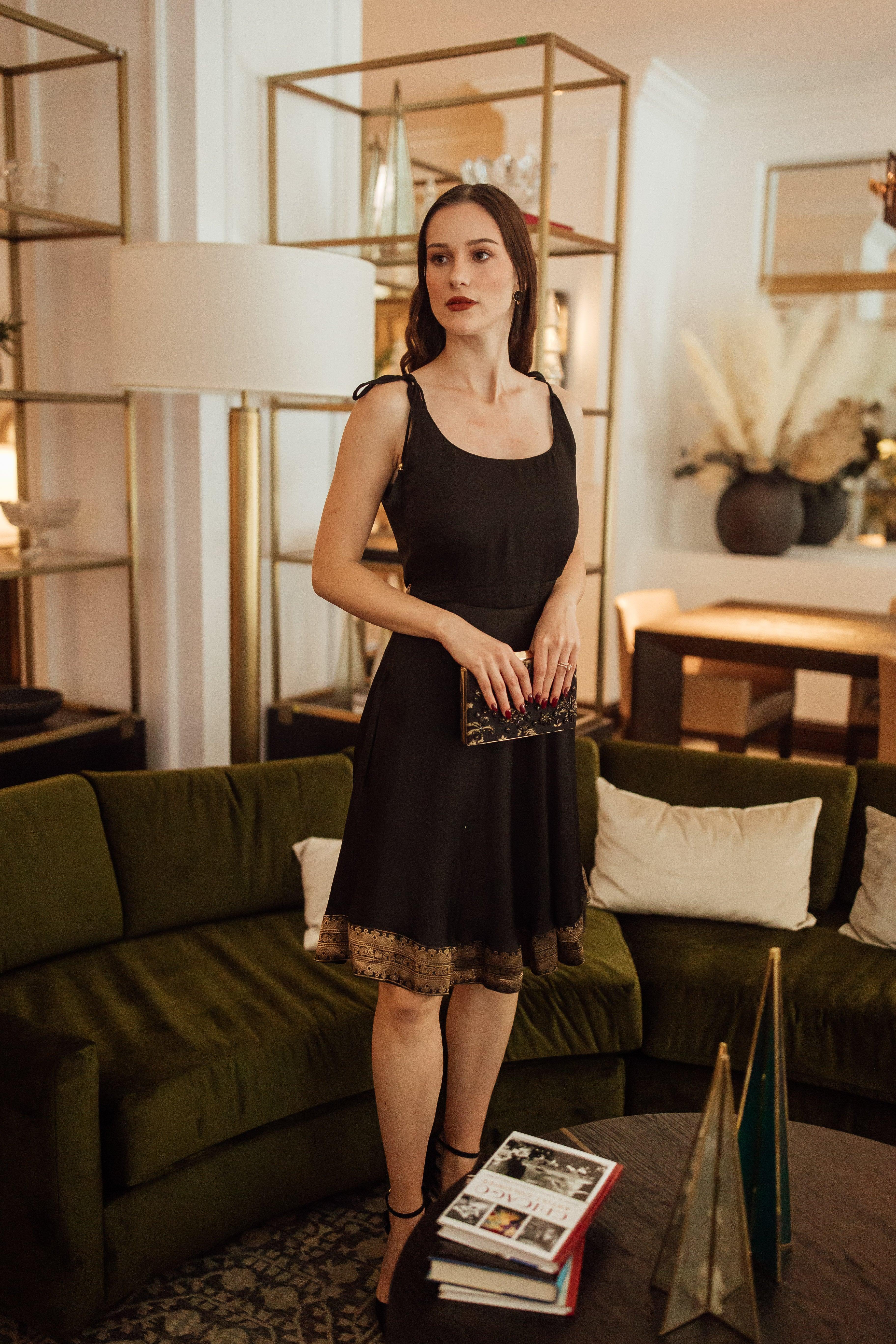 Black silk mini dress with Banarasi silk hem, sleeveless, and a golden bow tie at the back.