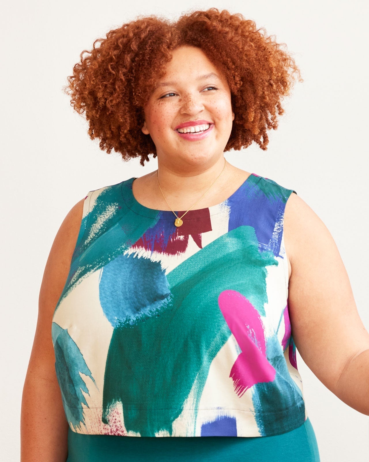 Woman wearing a colorful sleeveless top with abstract patterns on a plain background. This top is the Thorndike Tank sewing pattern from Cashmerette.