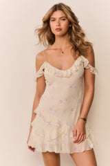 Woman wearing a light-colored off the shoulder dress with floral patterns on a plain background