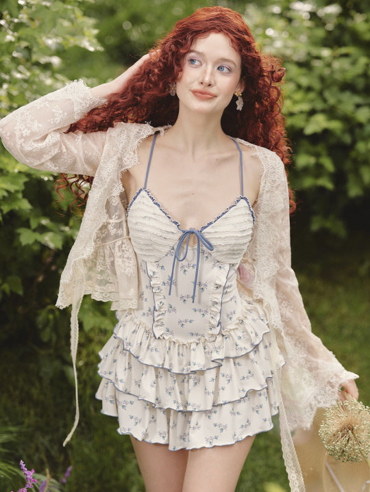 Wearing a tiered coquette floral dress with a ruched bodice and ribbon tie, the model smiles softly in a dreamy fairycore garden setting.