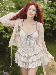 Wearing a tiered coquette floral dress with a ruched bodice and ribbon tie, the model smiles softly in a dreamy fairycore garden setting.