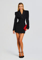 Model wearing a black double breasted blazer dress, holding a red clutch and wearing black heels