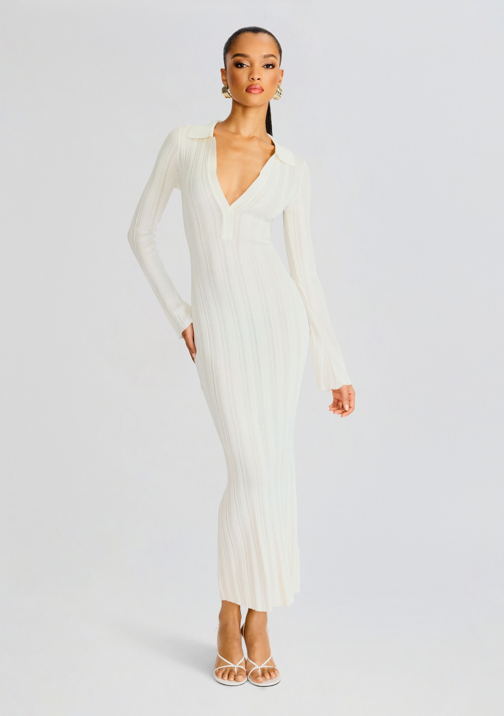 Full-length shot of a model wearing a white rib knit maxi dress with a deep V neckline and long sleeves.