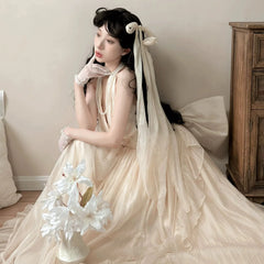 Woman in a flowing beige dress with a large bow sitting on a wooden floor.