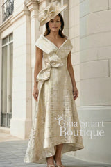 Gabriela Sanchez gold and Crudo metallic dress with dipped hem, statement waist bow, and matching hat – elegant Mother of the Bride outfit.