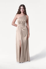 A woman wears the TH&TH Greta Bridesmaid Dress in Champagne Sky Satin, a one-shoulder gown with a gathered waist and thigh-high slit, standing against a plain white background.