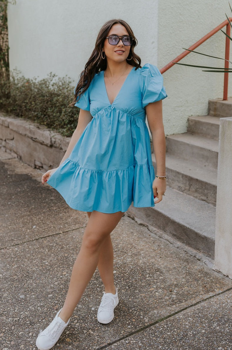 Full body view of female model wearing the Stephanie Light Blue Short Puff Sleeve Mini Dress which features light blue light weight fabric, mini length, flared skirt, plunge neckline, short puff sleeves, tie closure in the back and monochrome side zipper with hook closure.