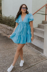 Full body view of female model wearing the Stephanie Light Blue Short Puff Sleeve Mini Dress which features light blue light weight fabric, mini length, flared skirt, plunge neckline, short puff sleeves, tie closure in the back and monochrome side zipper with hook closure.