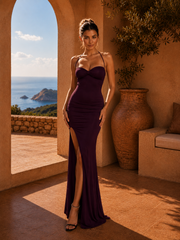 Woman in a purple dress standing in a sunlit room with a scenic view of the ocean.
