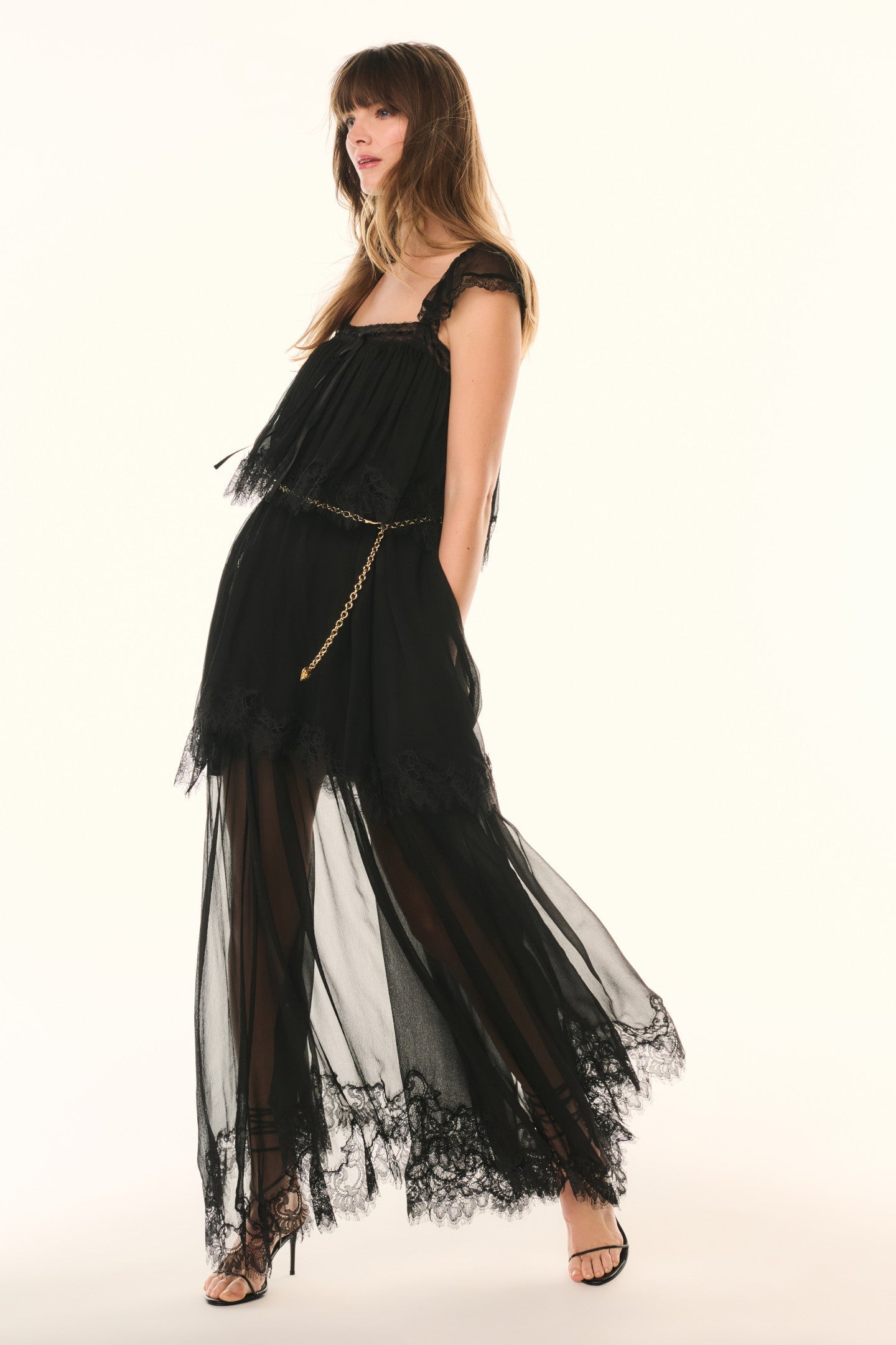 Woman wearing a black evening gown with sheer overlay on a white background