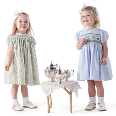 Two girls in smocked dresses at miniature tea table with silver tea set