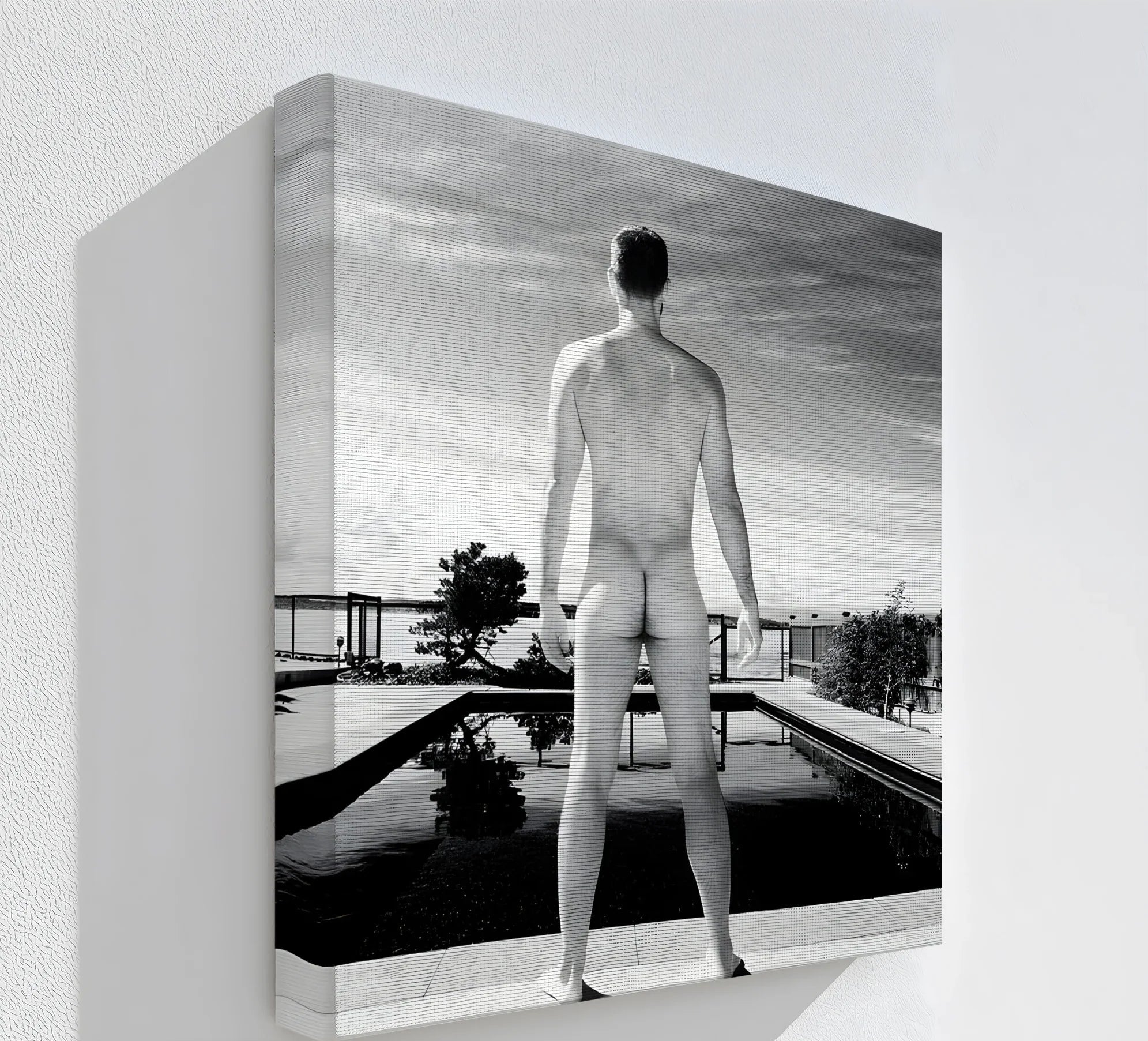 Negative space surrounds a black and white canvas wall art print depicting a nude male figure at a modern pool, emphasizing the stillness.