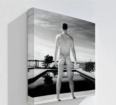 Negative space surrounds a black and white canvas wall art print depicting a nude male figure at a modern pool, emphasizing the stillness.