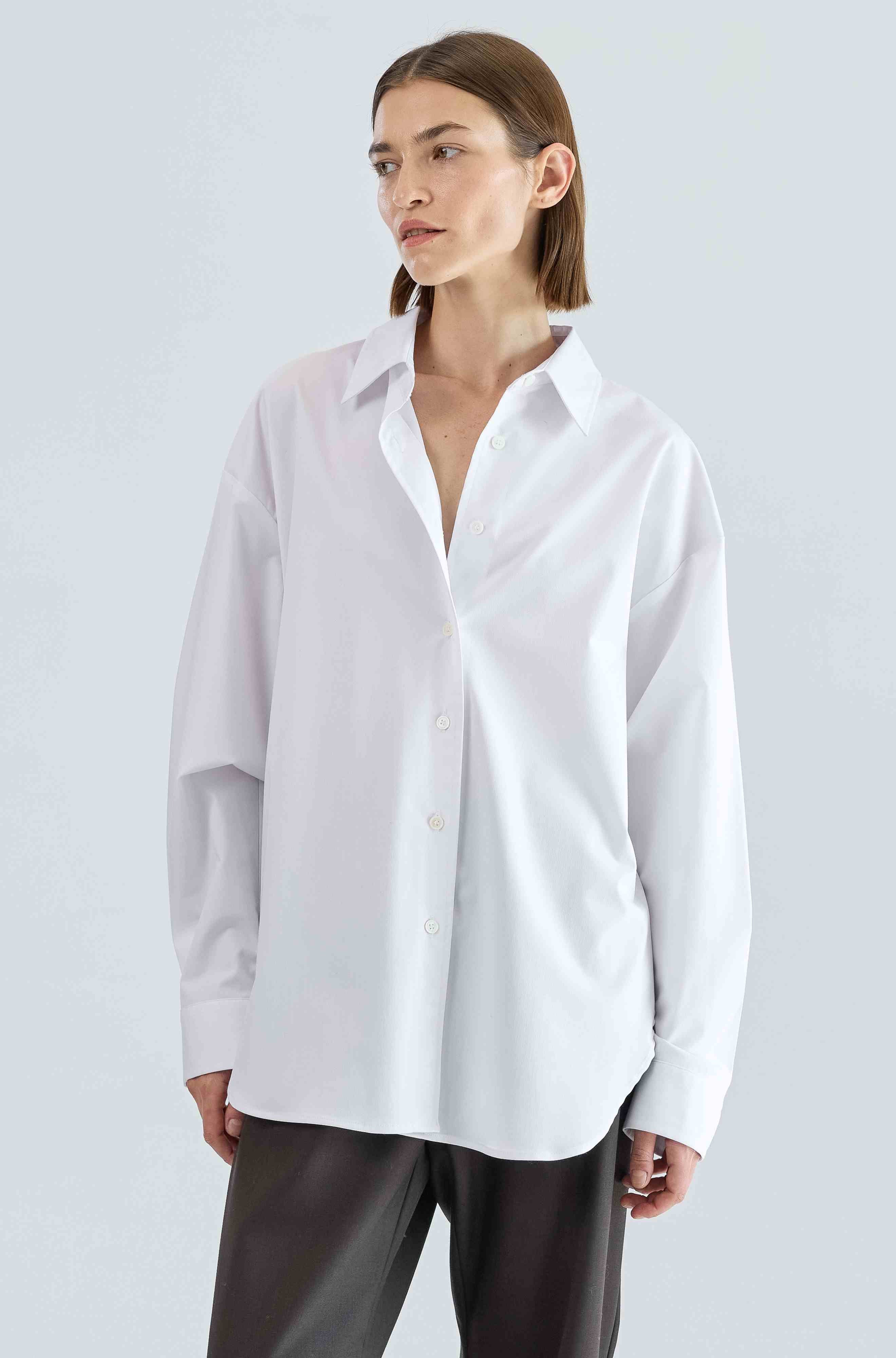 Woman wearing a white shirt and dark pants on a light gray background