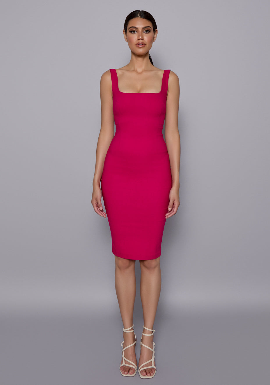 Model wearing the VSPR Zada Cerise Midi Dress featuring a square neckline, wide shoulder straps, and bodycon pencil silhouette, set against a minimalist grey studio backdrop.