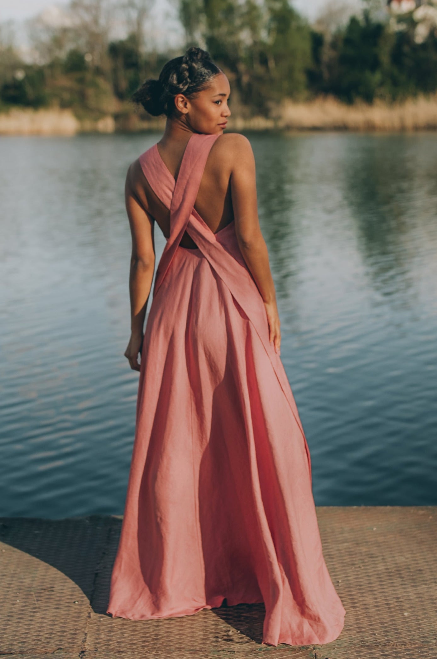 Woman wearing a pink cross-back linen dress standing by the water