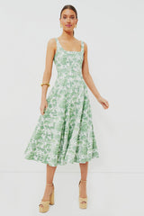 A woman wearing a STAUD Clover Toile Wells Dress—a sleeveless green and white corset-style midi with a square neckline—paired with gold hoop earrings and platform heels.