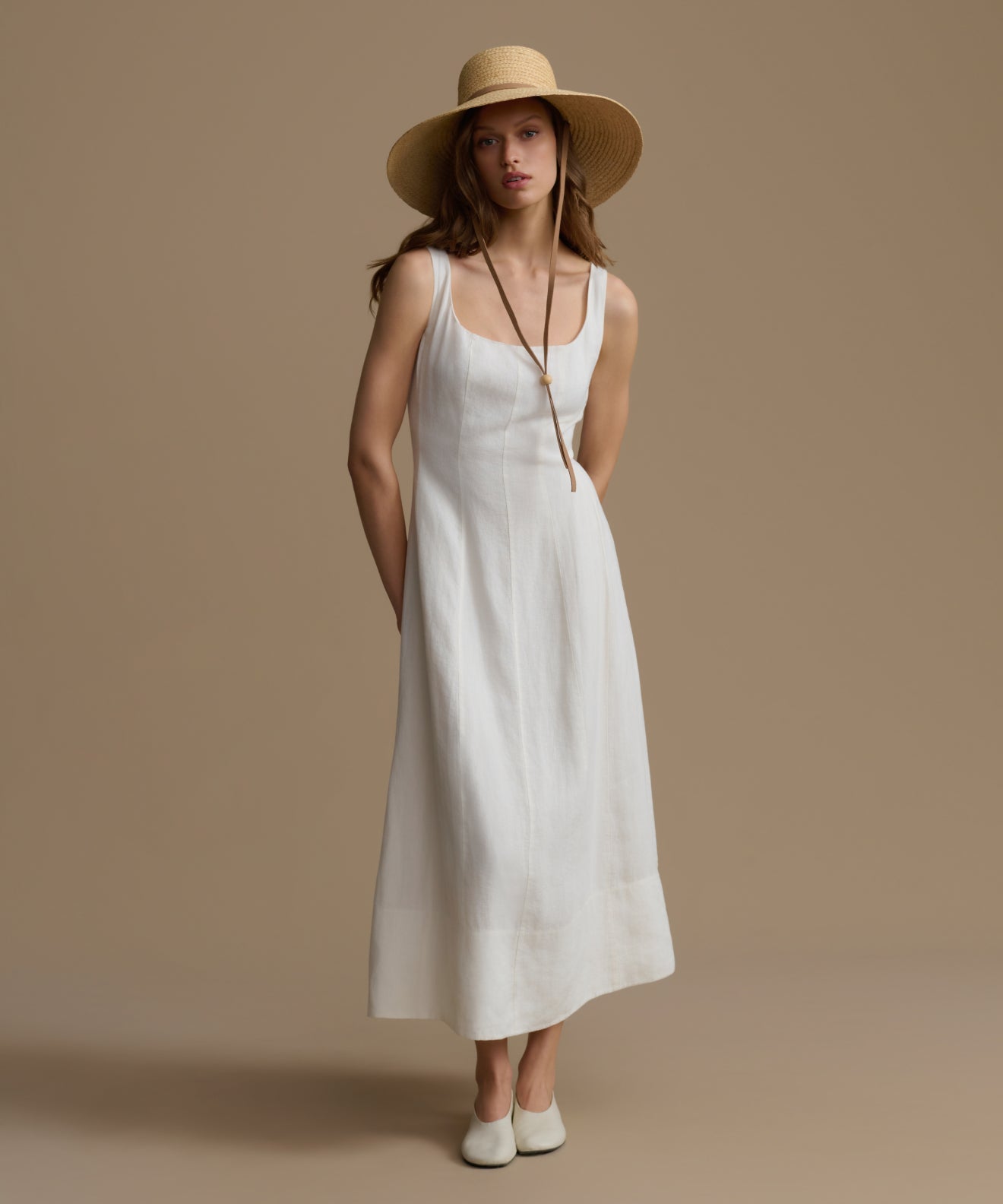Woman wearing a white dress and beige hat against a brown background