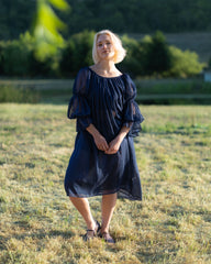 Woman wearing a navy blue chiffon chemise with puff sleeves standing outdoors in a sunlit field