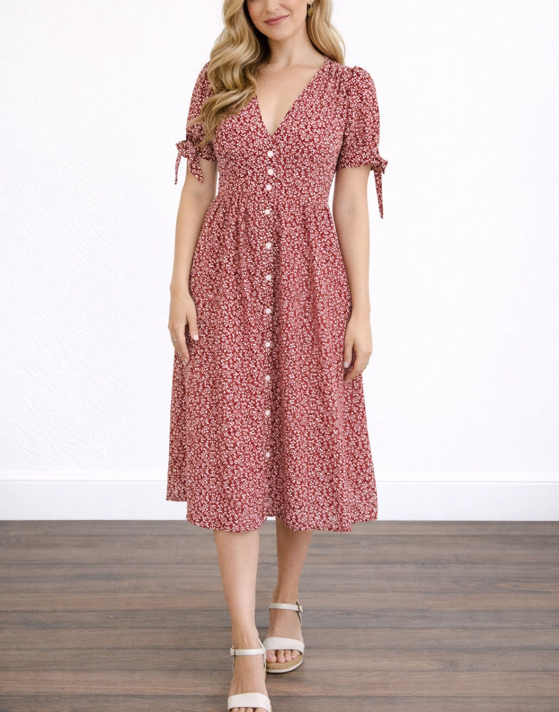 Woman wearing a red floral Tie Sleeve Button Front Midi Dress against a plain wall.