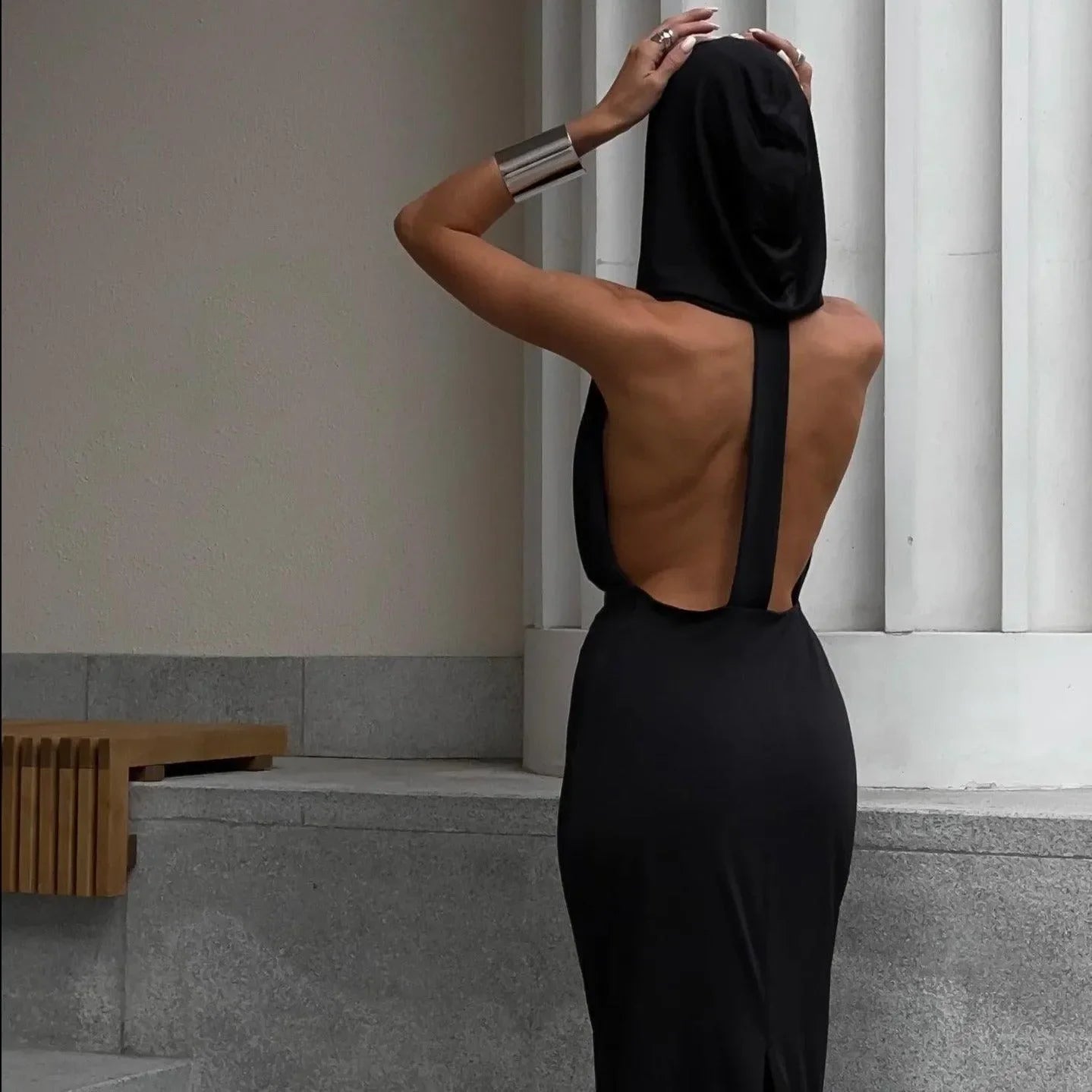 Black backless maxi dress with a hood, elegantly worn off the shoulders, perfect for summer evenings or beach outings.
