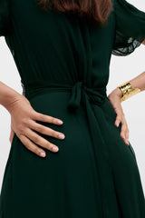 Wearing the Corrine - Diana Embellishment Forest Green dress, a person stands with hands on hips, highlighting manicured nails and a gold bracelet.