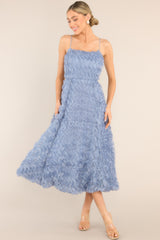 This blue dress features a rounded neckline, thin straps, a functional zipper down the back, and a wavy, ruffled overlay.
