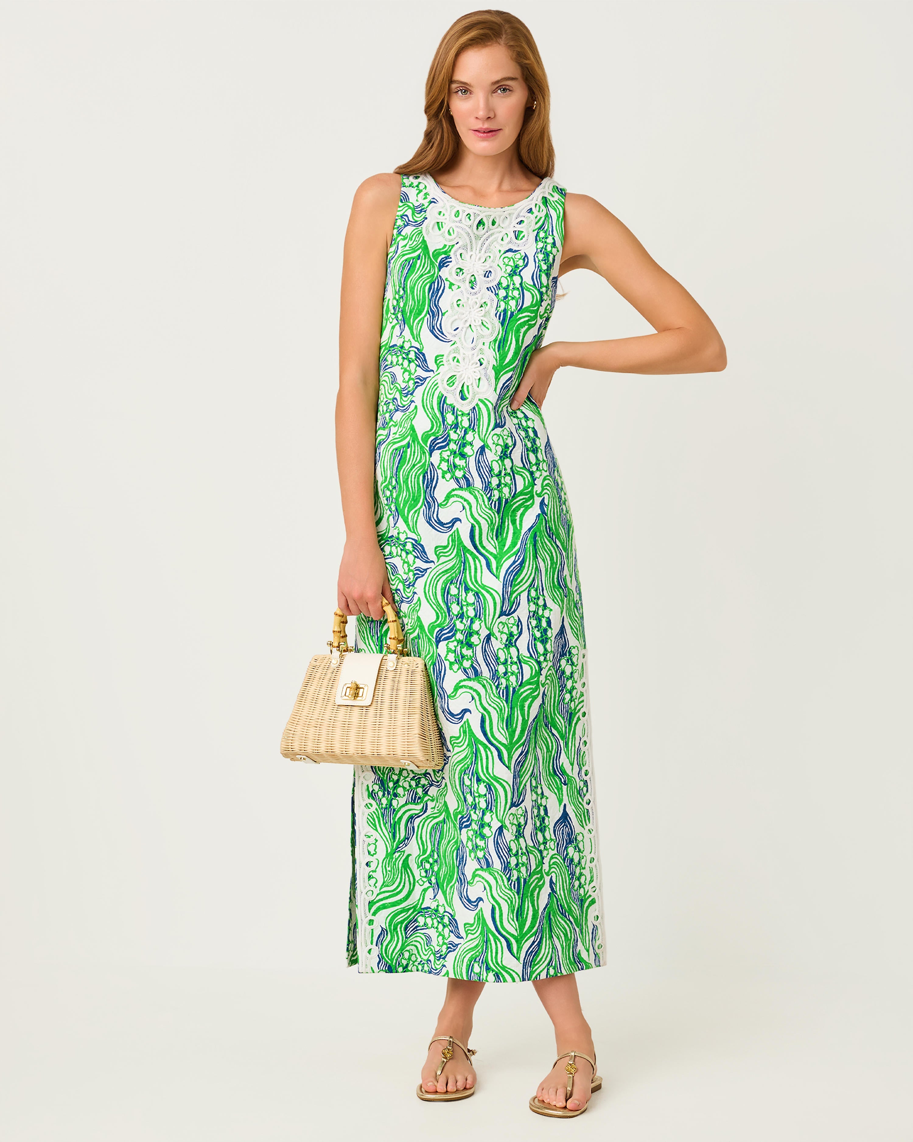 Woman wearing a green and white patterned dress holding a beige handbag on a white background