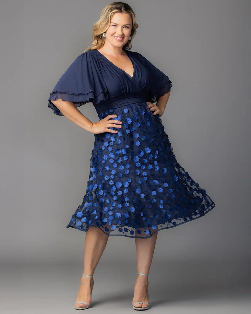 Pretty Petals Mesh Cocktail Dress in Navy Blooms. Model in a black and blue  floral cocktail dress posing in front of a grey background.