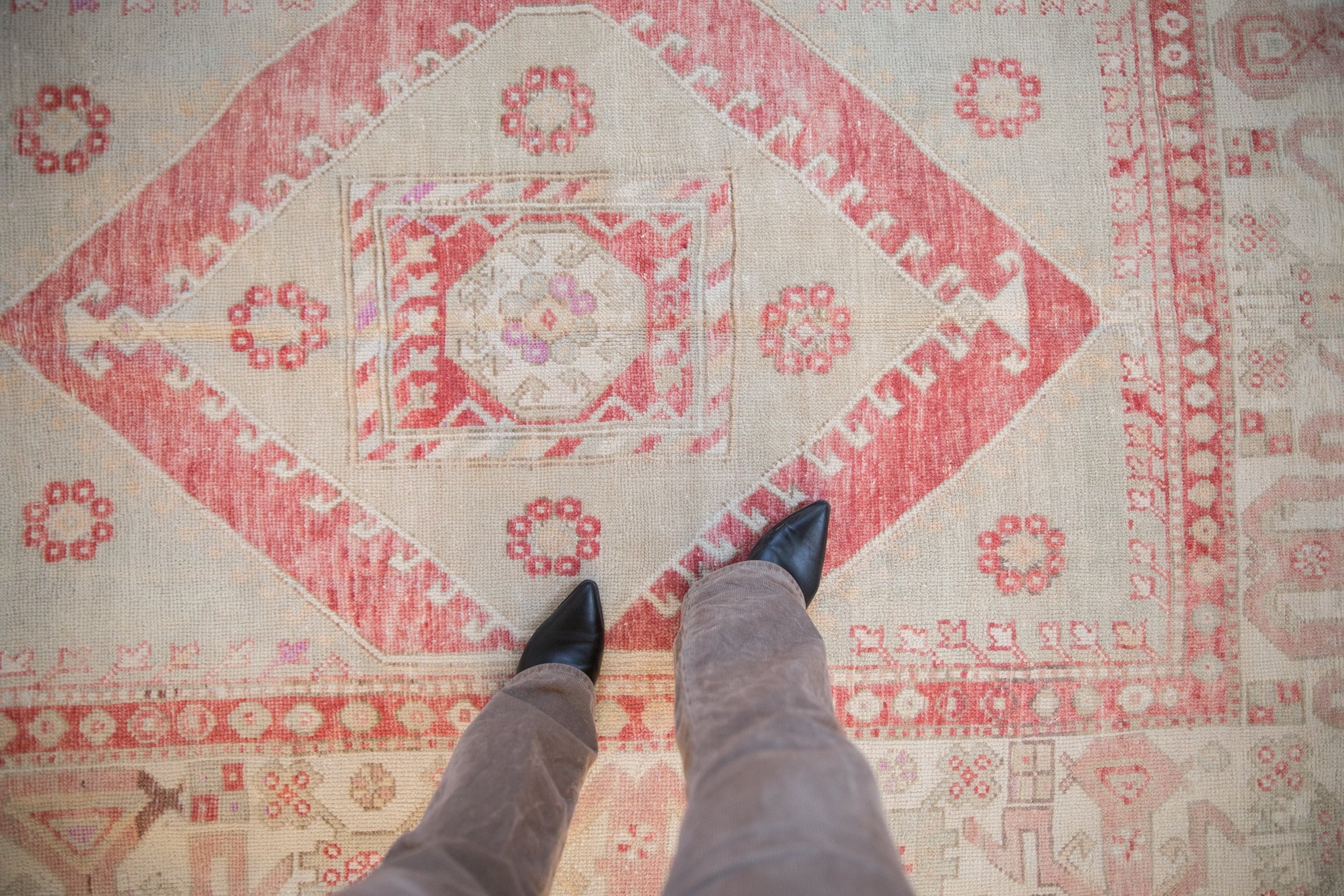 Personal perspective of a distressed Oushak rug's worn texture and red and ivory diamond medallion.